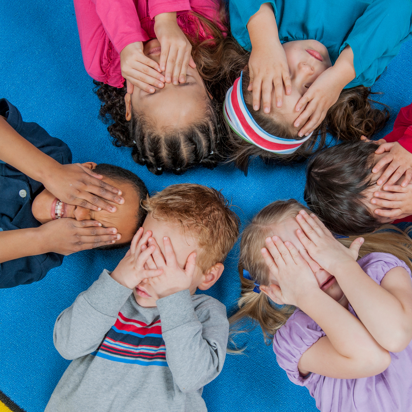 Six diverse young children covering their eyes.