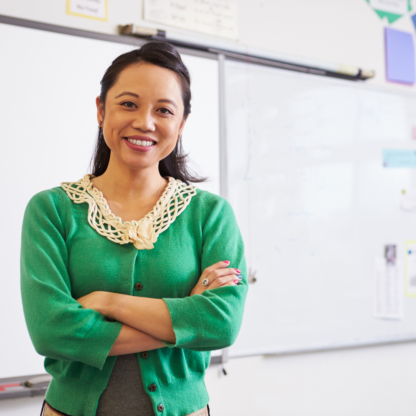A teacher smiles at the camera in front of a whiteboard.